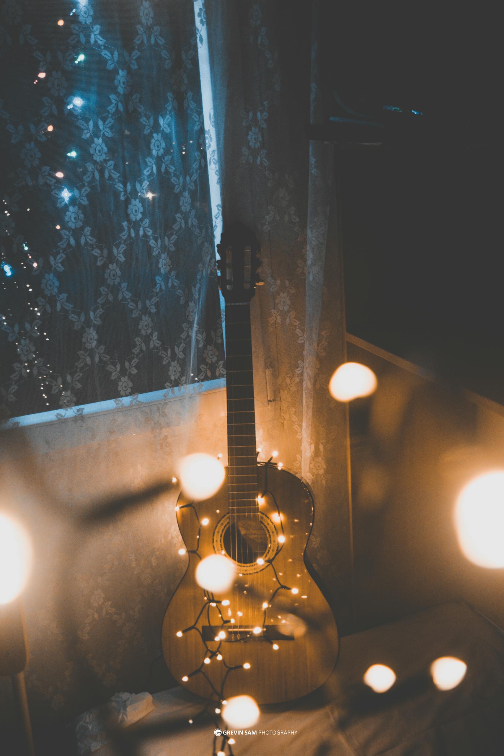 Acoustic guitar adorned with warm string lights creating a cozy indoor atmosphere.